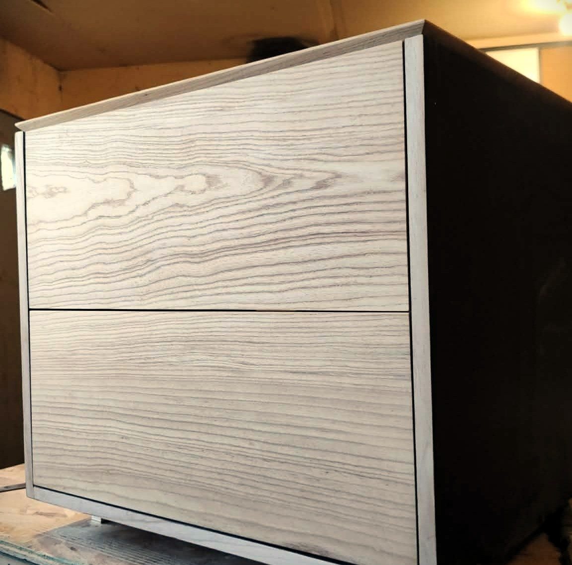 Two-drawer ash nightstand in progress with black side panel, built in an Edmonton shop.