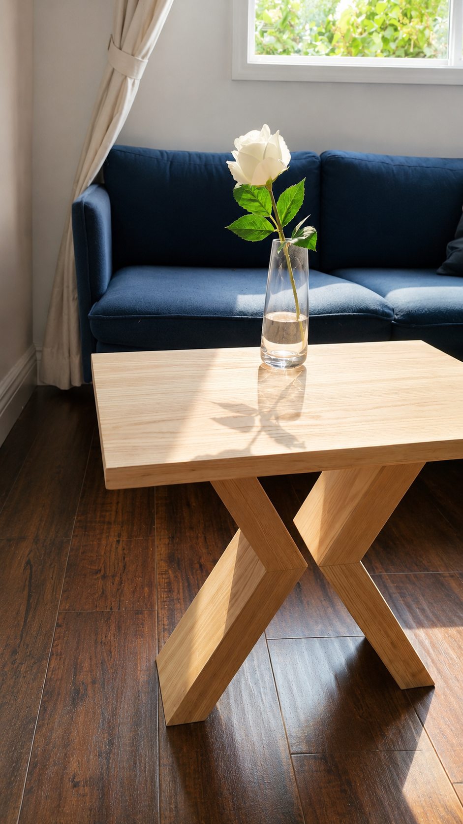 Handmade ash side table with crossed base in front of a blue sofa.